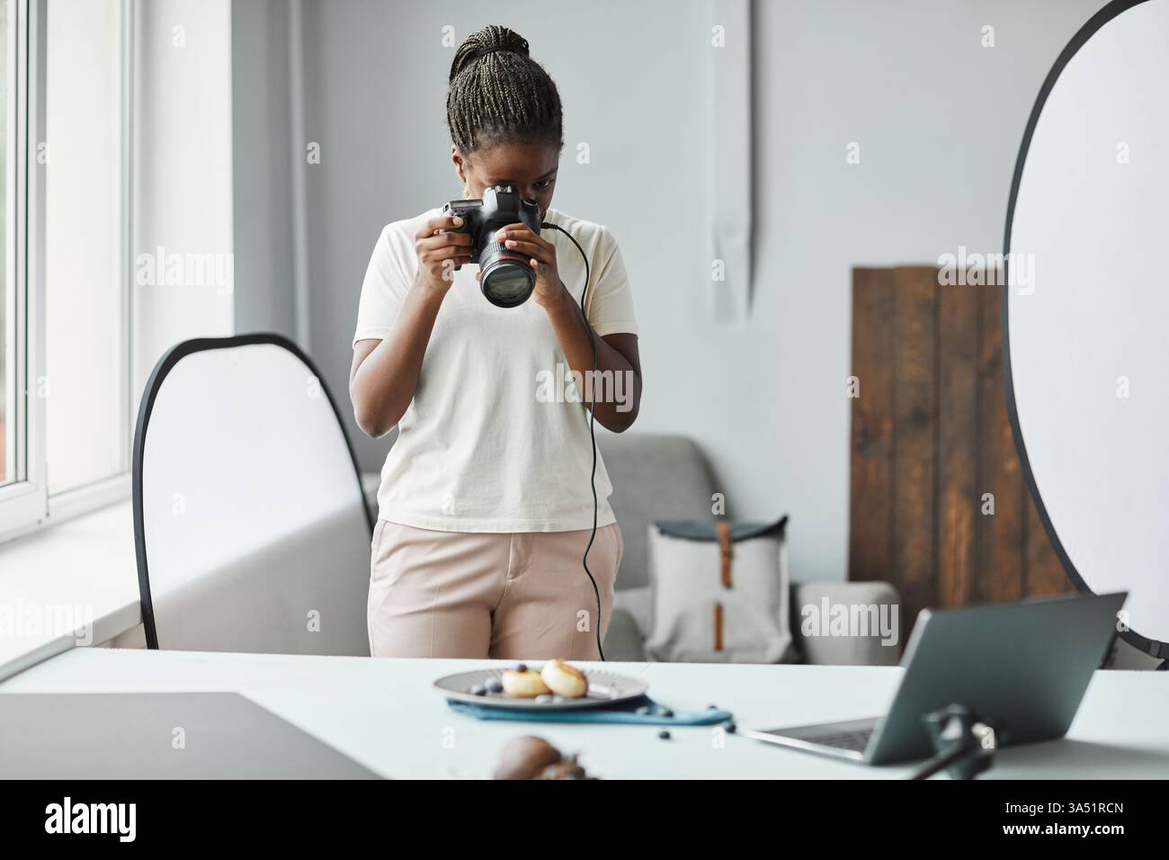 Portrait minimal d'une jeune femme afro-américaine photographe dans un studio de création de photographie culinaire. L'espace de copie rend cette image idéale pour les portefeuilles, la marque et la publicité dans le style alimentaire. Parfait pour les contextes de création, de photographie et de prise de vue de produits. Banque D'Images