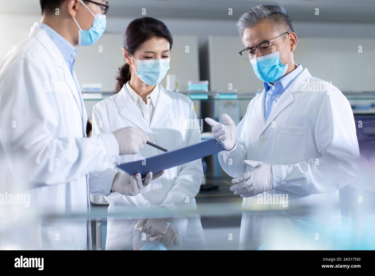 Trois chercheurs dans un laboratoire discutent des résultats, mettant en évidence le travail d'équipe en science et en recherche médicale. Vêtus de blouses de laboratoire au milieu de matériel de biotechnologie, ils analysent les données liées à la recherche génétique. Banque D'Images