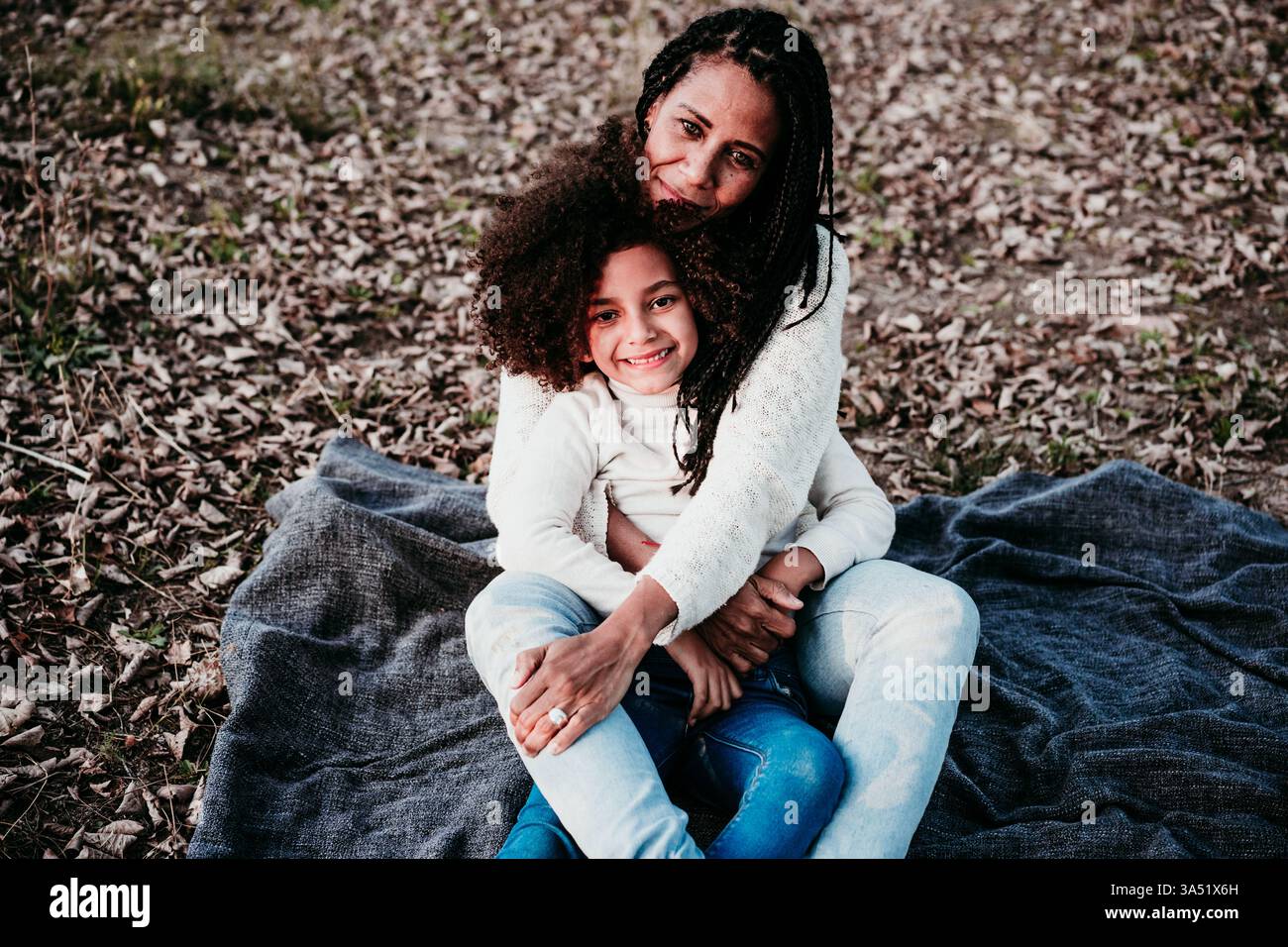Mère hispanique avec sa fille afro se relaxant en plein air en automne, parmi les arbres et les feuilles. Le moment chaleureux en famille communique la convivialité, le bonheur et l'amour dans un cadre de parc. Parfait pour la famille, les parents et les campagnes de style de vie multiculturel. Banque D'Images