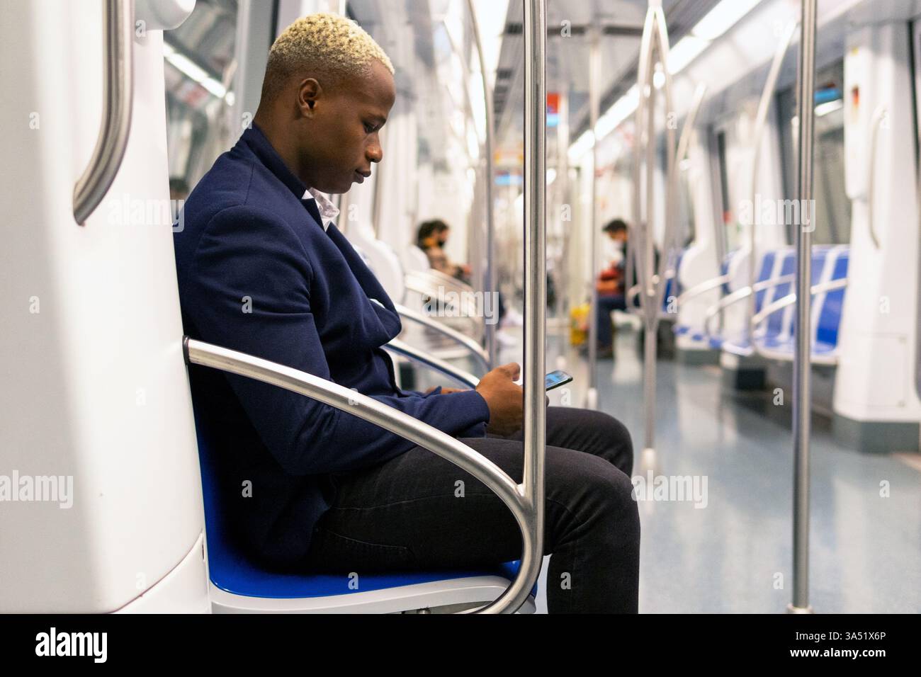 Portrait urbain d'un homme noir dans la vingtaine à l'aide d'un smartphone dans le métro. Il est assis dans une calèche en tenue élégante, illustrant les trajets quotidiens modernes et la connectivité numérique dans la vie urbaine. Banque D'Images