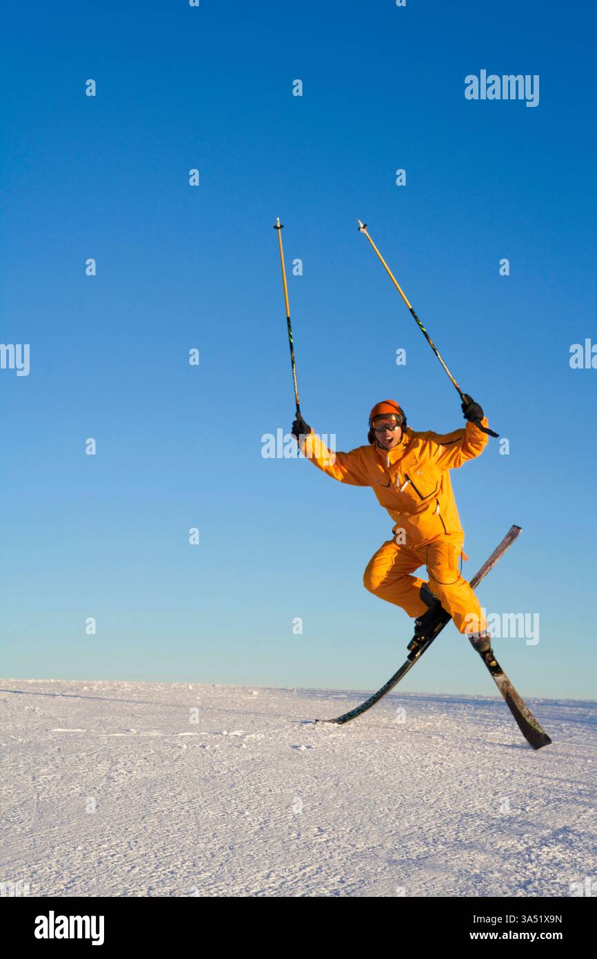 Jeune homme chinois posant avec du matériel de ski sur une pente enneigée dans une station de ski. Ciel dégagé et paysages hivernaux encadrent un mode de vie actif et sain et les sports d'hiver. Idéal pour les voyages, les sports d'hiver et les campagnes de loisirs en plein air. Banque D'Images