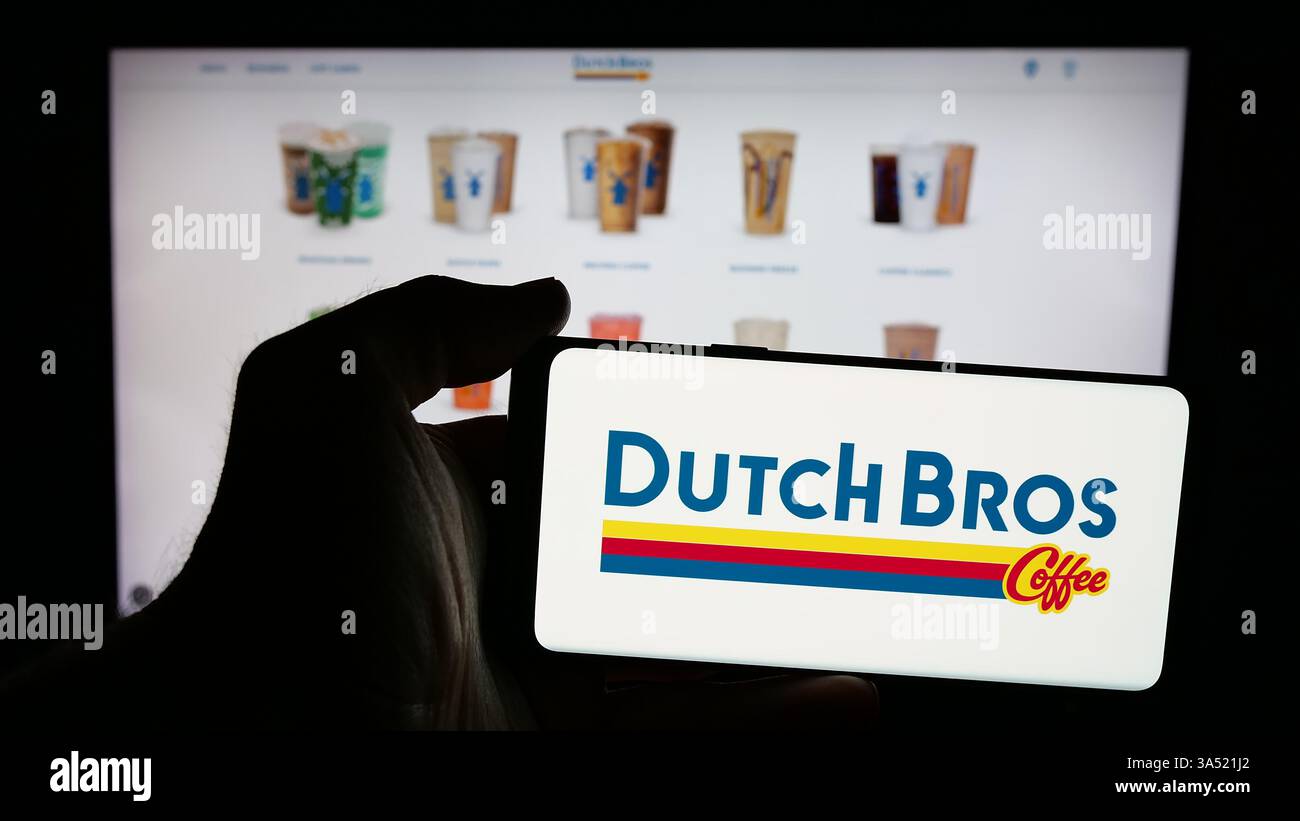 Personne tenant le téléphone portable avec le logo de la société de chaîne de café américaine Dutch Bros Inc sur l'écran en face de la page Web. Banque D'Images