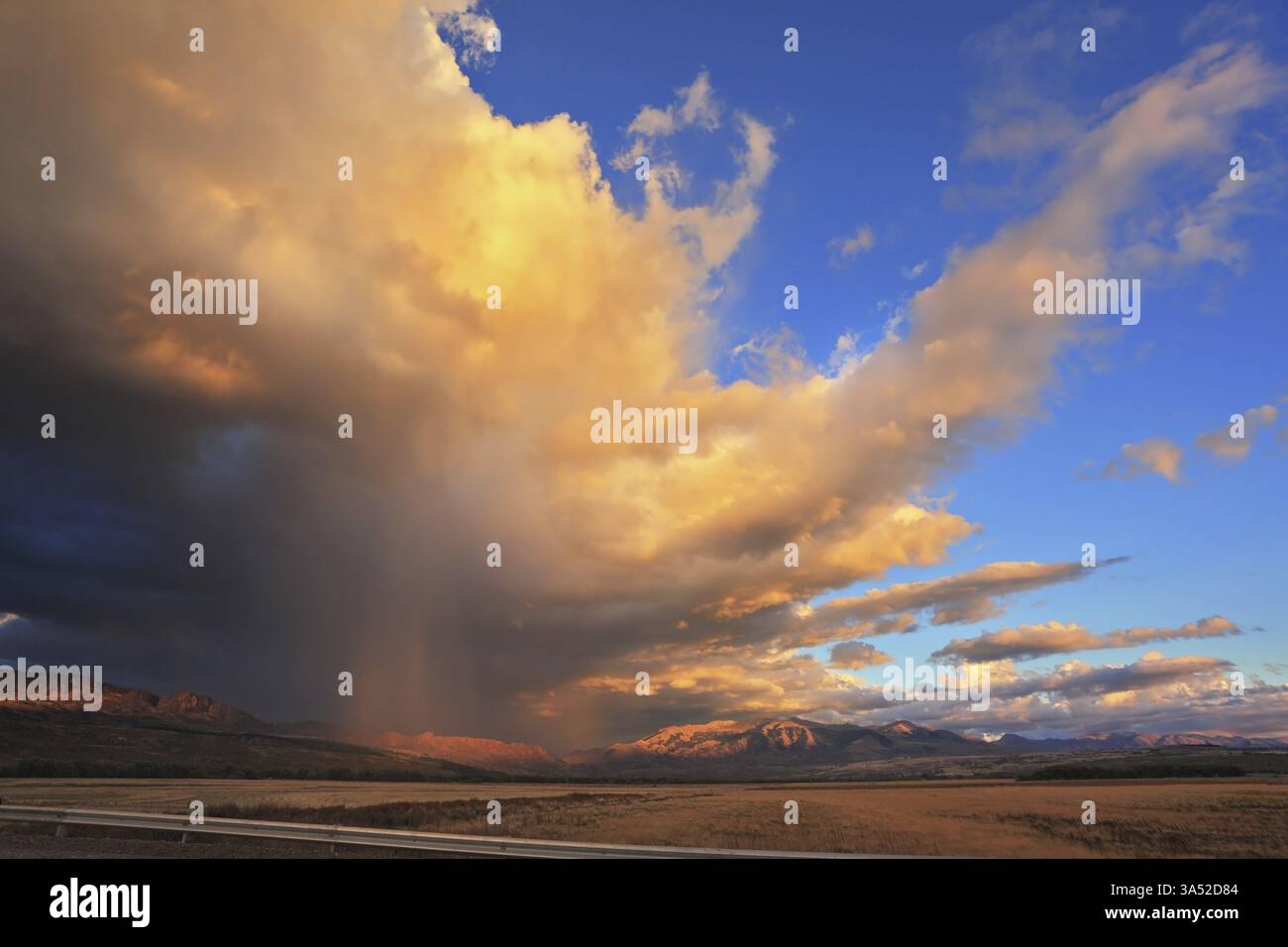 Pluie estivale. Incroyablement beau énorme nuage de pluie illuminé le soleil couchant. Jet d'eau d'orage brillant orange. Nuage pend au-dessus de la route de gravier Banque D'Images