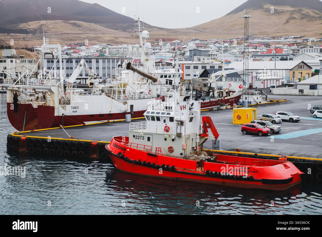 Vestmannaeyjar, Islande - 6 avril 2017 : une vue panoramique d'un port avec des bateaux de pêche, un remorqueur rouge et une ville côtière en arrière-plan surr Banque D'Images