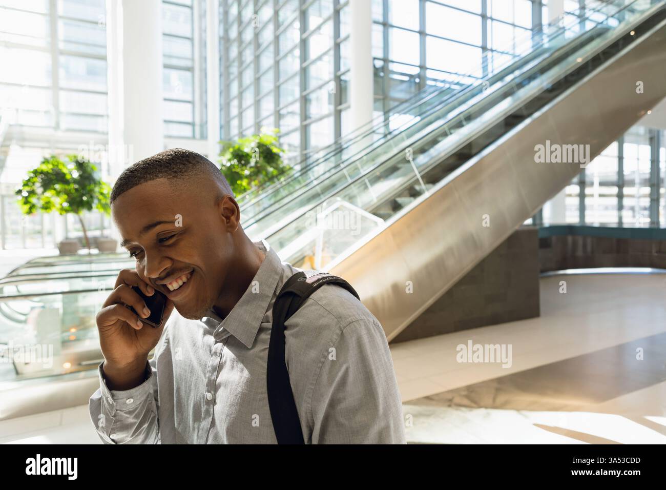 Homme d'affaires parlant sur smartphone, souriant tout en marchant dans le centre de conférence moderne, espace de copie Banque D'Images
