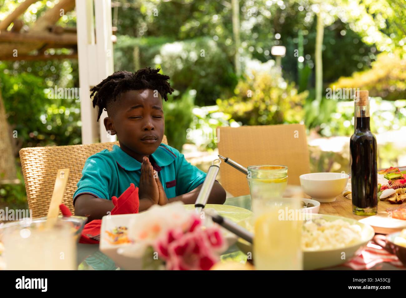 Enfant priant à la table de dîner familiale en plein air, entouré par la nourriture et la nature Banque D'Images