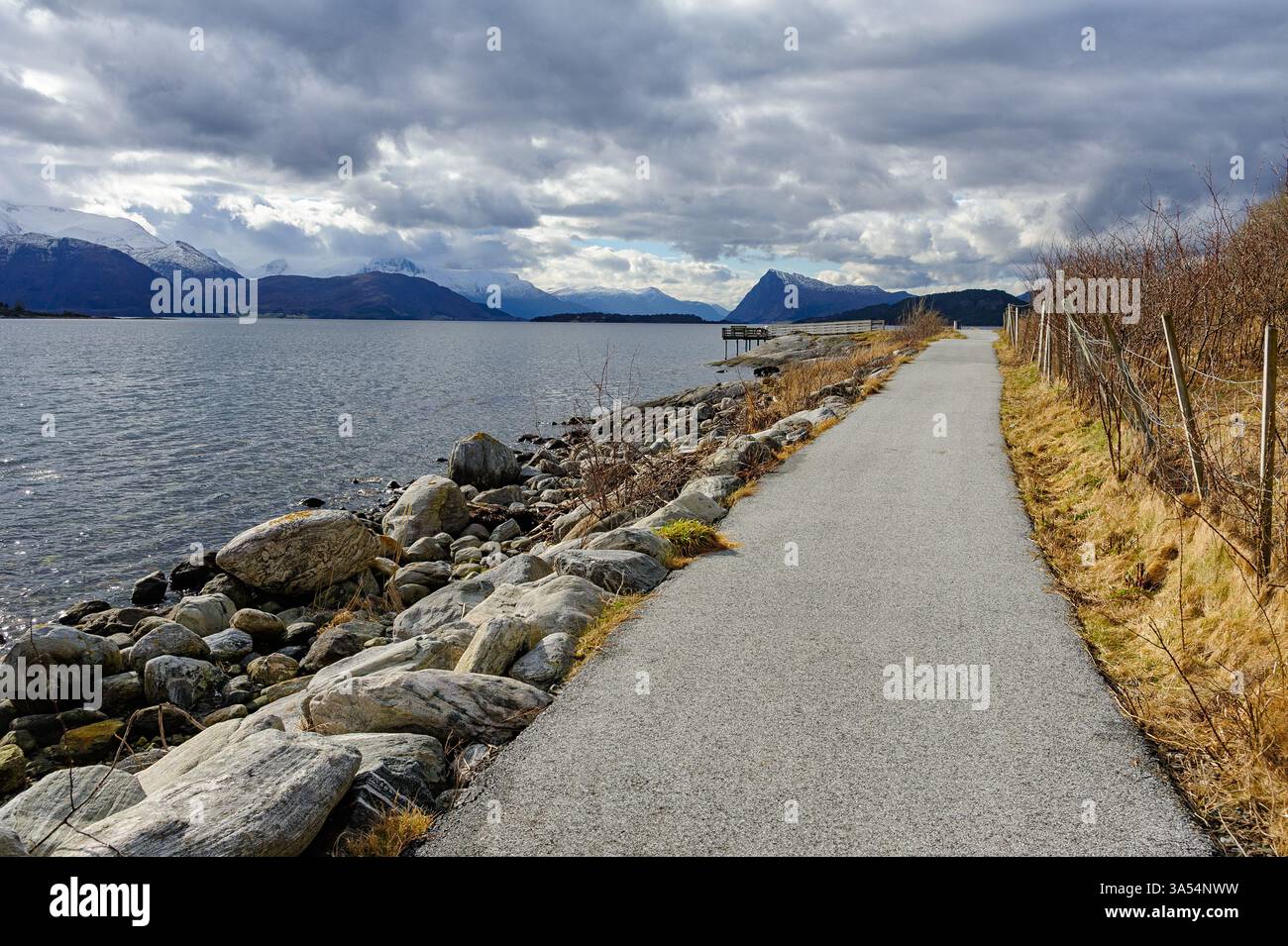 Profitez d'une promenade paisible le long d'un sentier balnéaire bordé de rochers et de montagnes sous un ciel nuageux spectaculaire. Banque D'Images