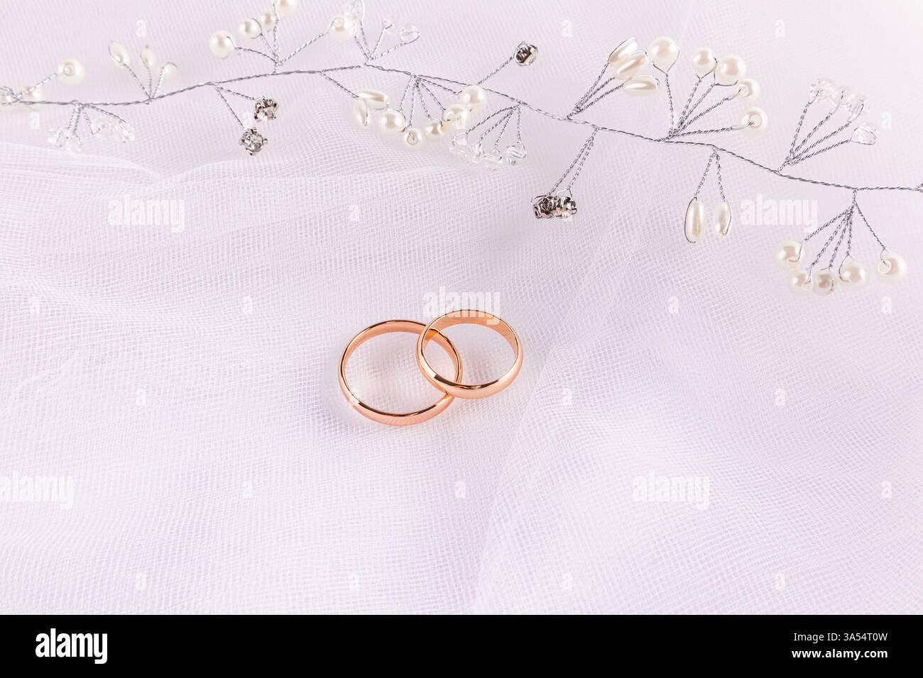 Un bel arrangement de mariage avec deux anneaux de mariage en or et une décoration de coiffure de perle et de strass. fond de tulle blanc Banque D'Images