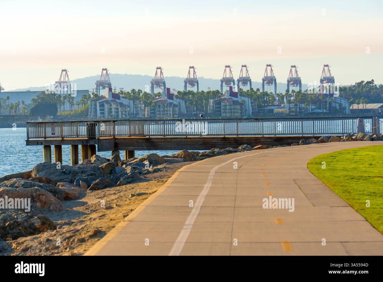 Long Beach, Californie - 11 janvier 2025 : sentier le long de l'eau mène à la jetée, aux maisons de bord de mer à proximité, et de grandes grues dans le port de long Beach. Banque D'Images