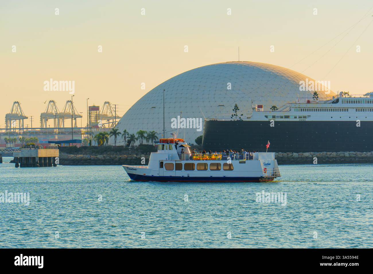 Long Beach, Californie - 11 janvier 2025 : bateau navigue dans les eaux calmes près de l'historique Queen Mary à long Beach, Californie, avec le skylin de la ville Banque D'Images