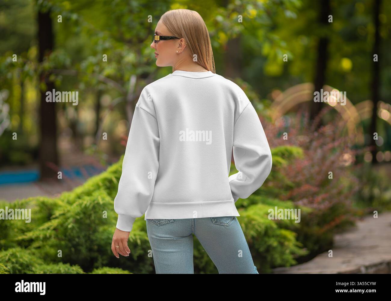 Maquette d'un sweat-shirt blanc sur une fille aux cheveux clairs en Jean bleu, sur le fond d'un parc, carré, vue arrière. Modèle d'un pu à la mode pour femmes Banque D'Images