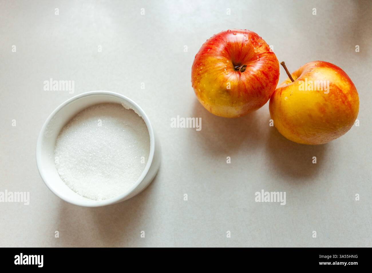 Sucre blanc dans un sucrier et deux pommes lavées sur la table Banque D'Images