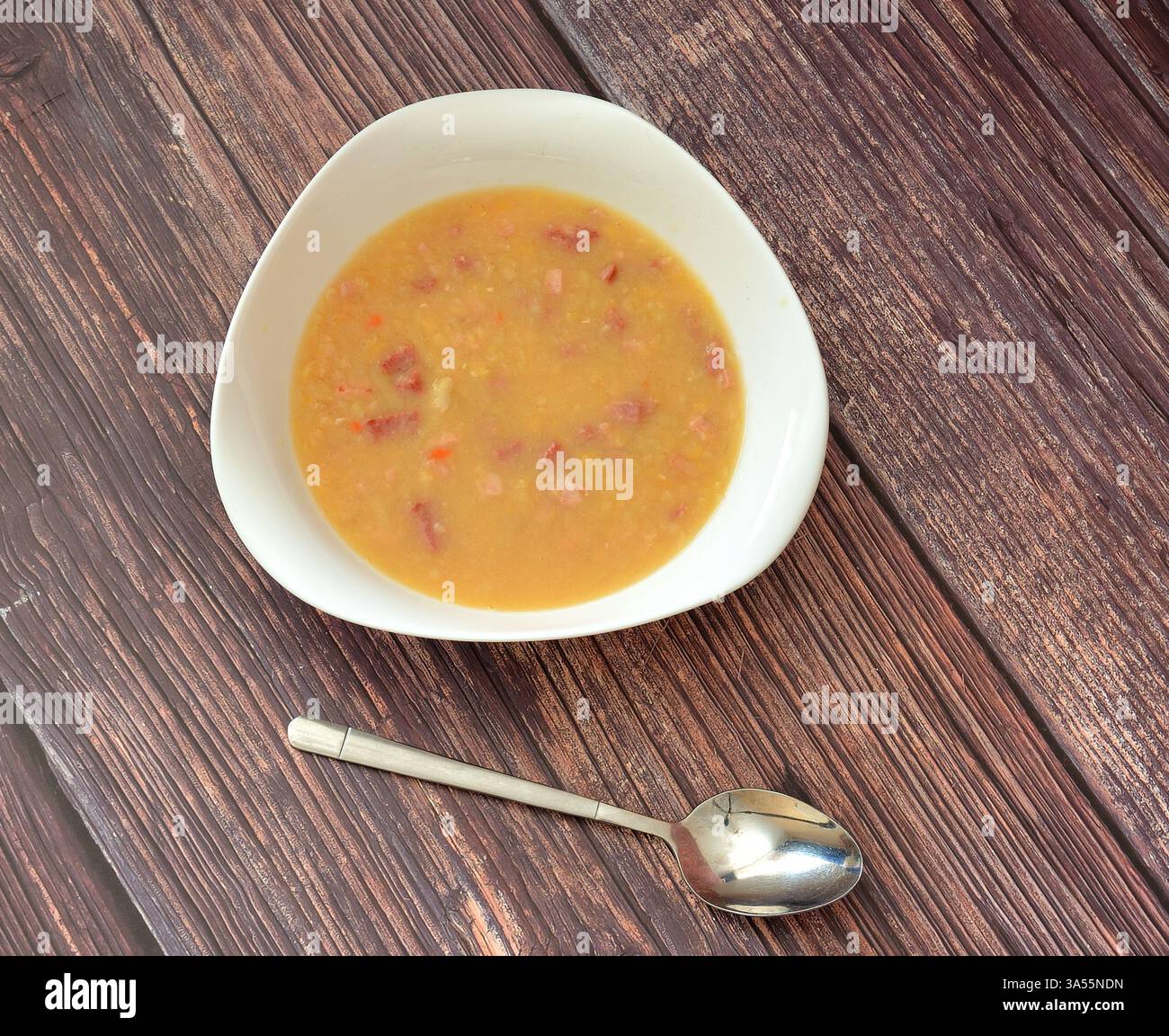 Une assiette de soupe de pois chaude et savoureuse avec des viandes fumées sur une table en bois, une cuillère à proximité. Vue de dessus, pose à plat. Banque D'Images