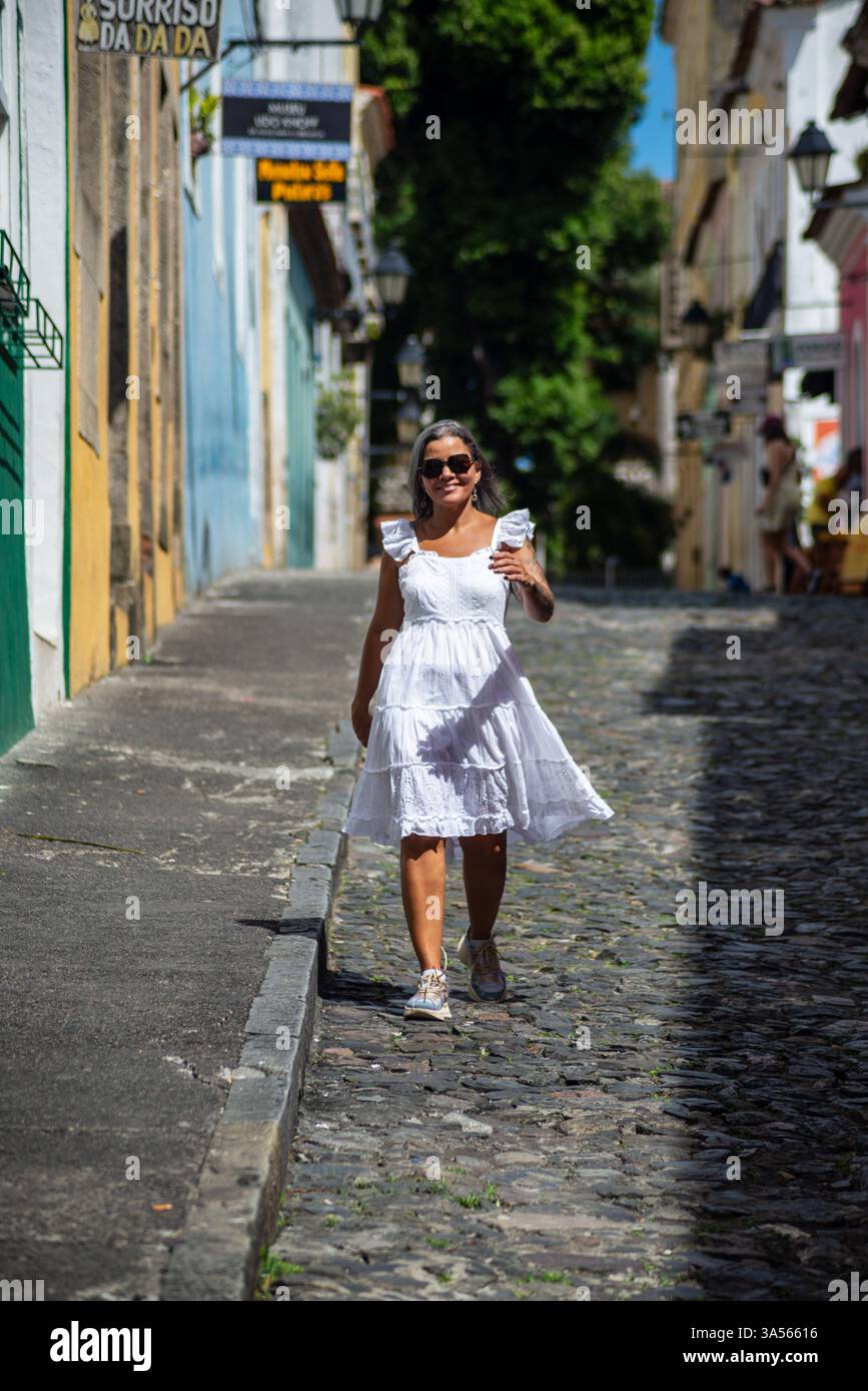 Belle femme portant une robe blanche et des lunettes de soleil, souriante et heureuse, marchant dans les rues contre les vieilles maisons. personne en voyage. Amérique du Sud. Banque D'Images