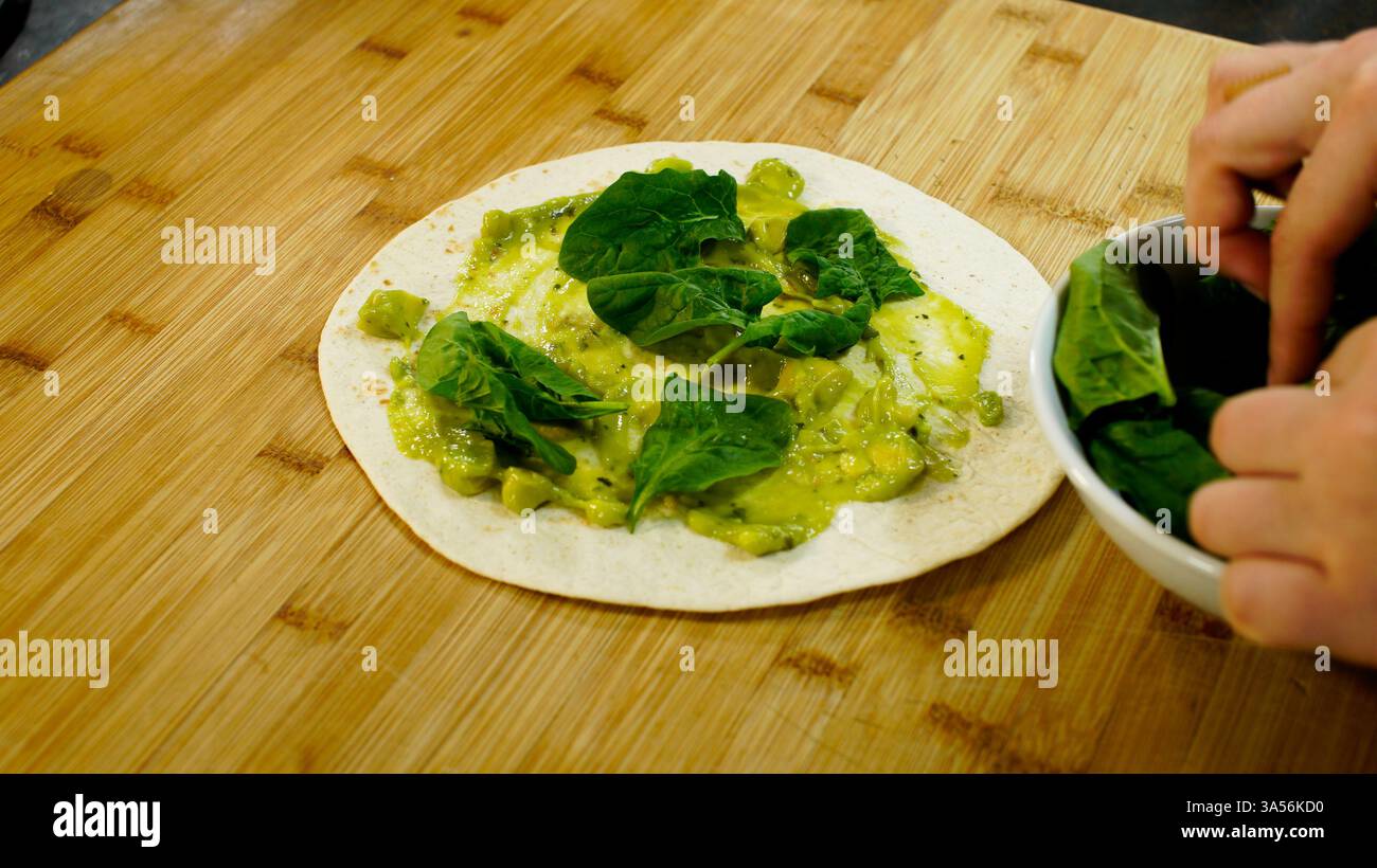Nourriture préparation d'un enveloppement tortilla de farine contenant de la salade, des légumes et de la viande sur un comptoir de cuisine en bois. Banque D'Images