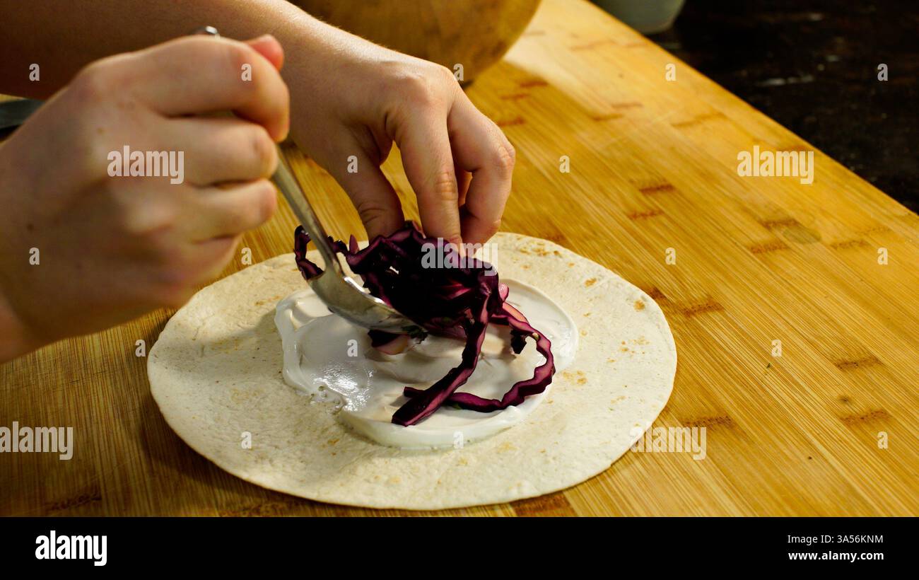Nourriture préparation d'un enveloppement tortilla de farine contenant de la salade, des légumes et de la viande sur un comptoir de cuisine en bois. Banque D'Images