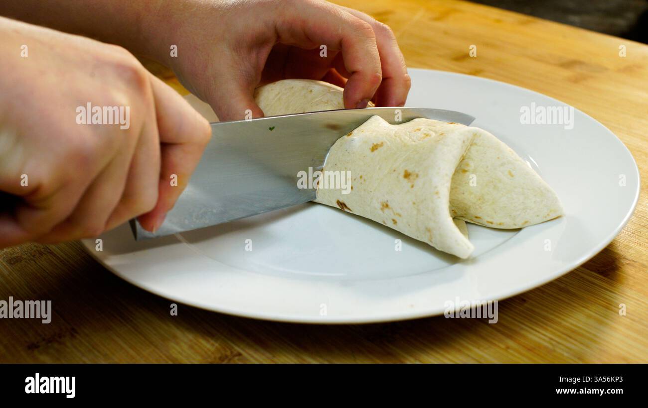 Nourriture préparation d'un enveloppement tortilla de farine contenant de la salade, des légumes et de la viande sur un comptoir de cuisine en bois. Banque D'Images