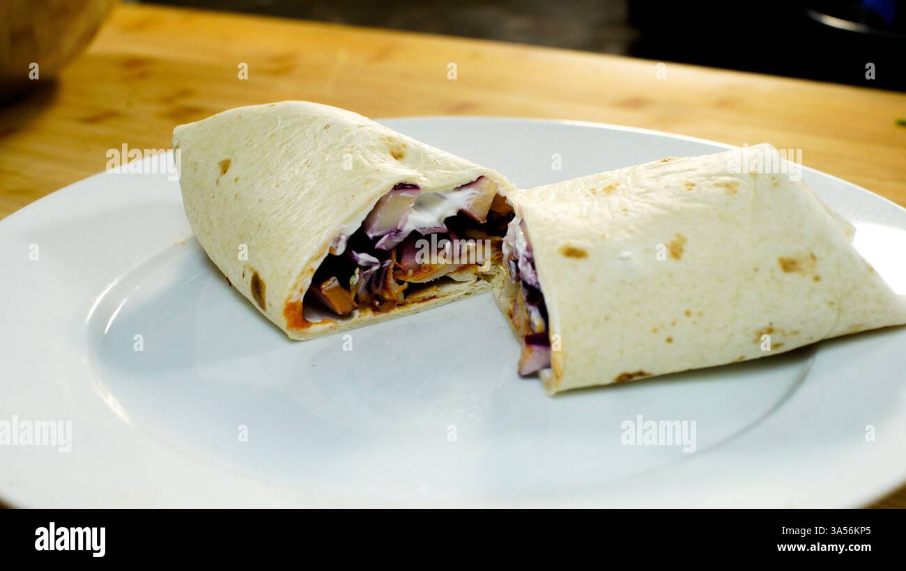 Taco, chimichanga, enchilada ou fajita servis et tranchés en deux sur une assiette blanche. Banque D'Images