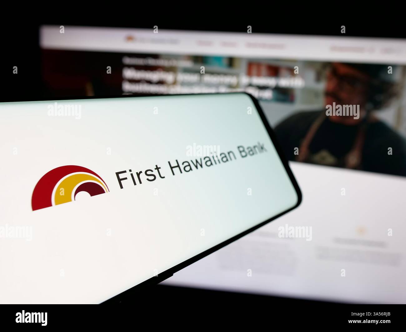 Stuttgart, Allemagne - 11-11-2024 : téléphone portable avec le logo de la société américaine de services financiers First Hawaiian Inc sur l'écran devant le site Web. Banque D'Images