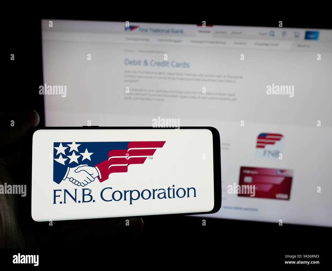 Stuttgart, Allemagne - 2024 : personne tenant un smartphone avec le logo de la société américaine FNB Corporation (First National Bank) sur l'écran devant le site Banque D'Images
