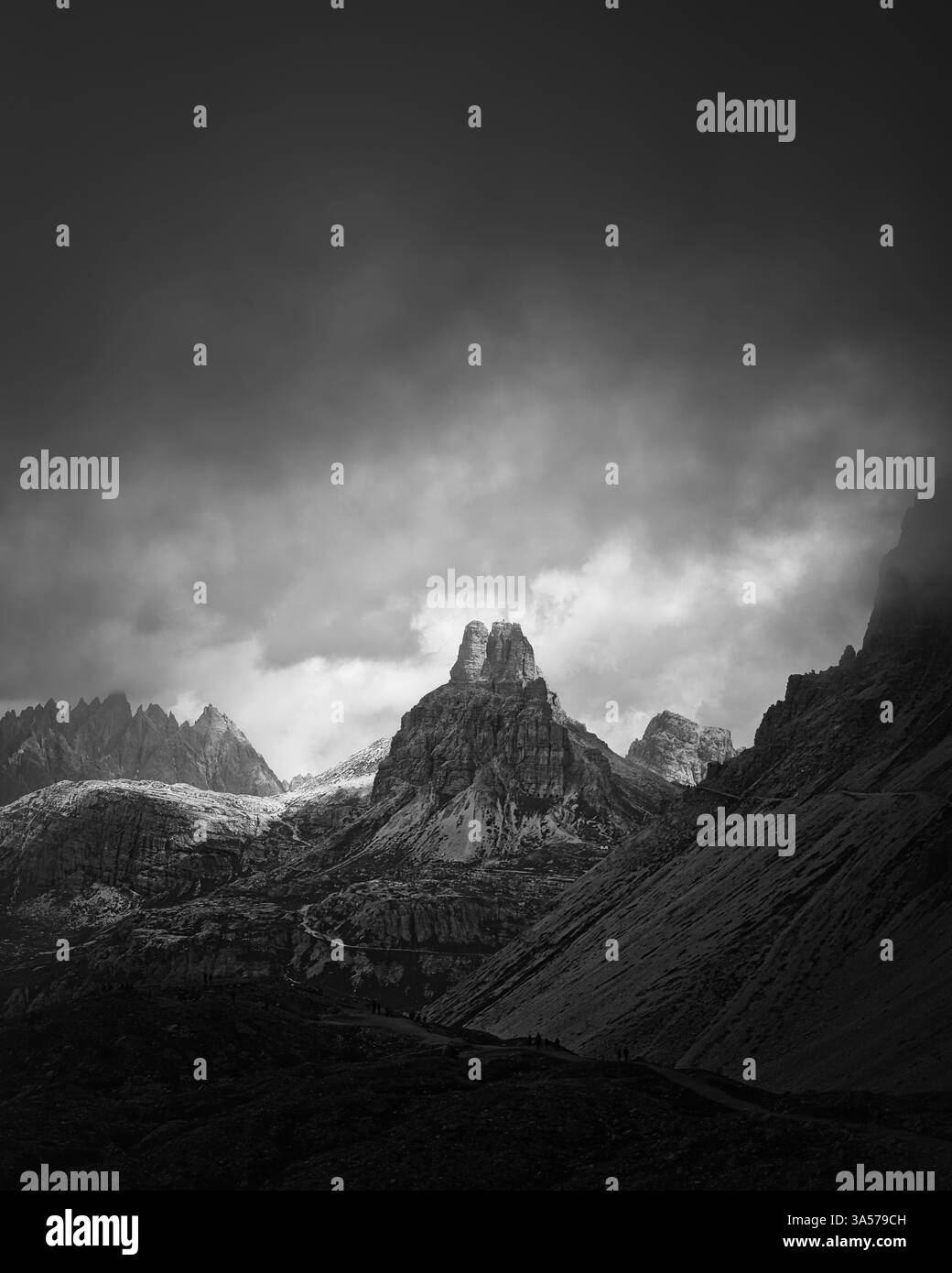 Vue en noir et blanc d'une tour rocheuse dramatique dans les Dolomites, en Italie, entourée de pics alpins escarpés sous un ciel nuageux menaçant. Banque D'Images