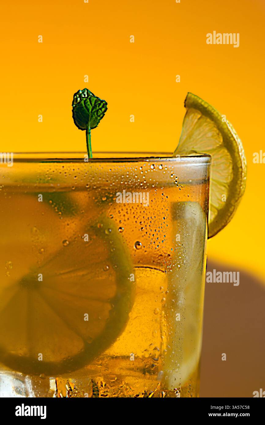 Un verre d'un thé glacé avec des tranches de citron vert et de citron dedans. La boisson est servie dans un verre avec des feuilles de menthe sur le dessus. Fond orange chaud. Banque D'Images