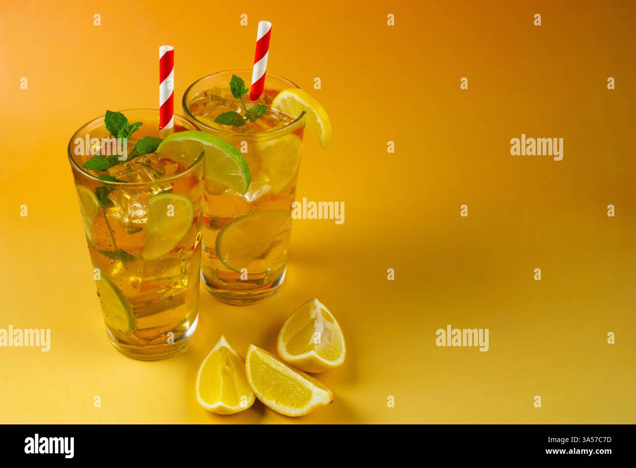 Deux verres de thé glacé avec des tranches de citron vert et de citron. La boisson est servie dans un verre avec des feuilles de menthe sur le dessus et des pailles blanches et rouges. Banque D'Images