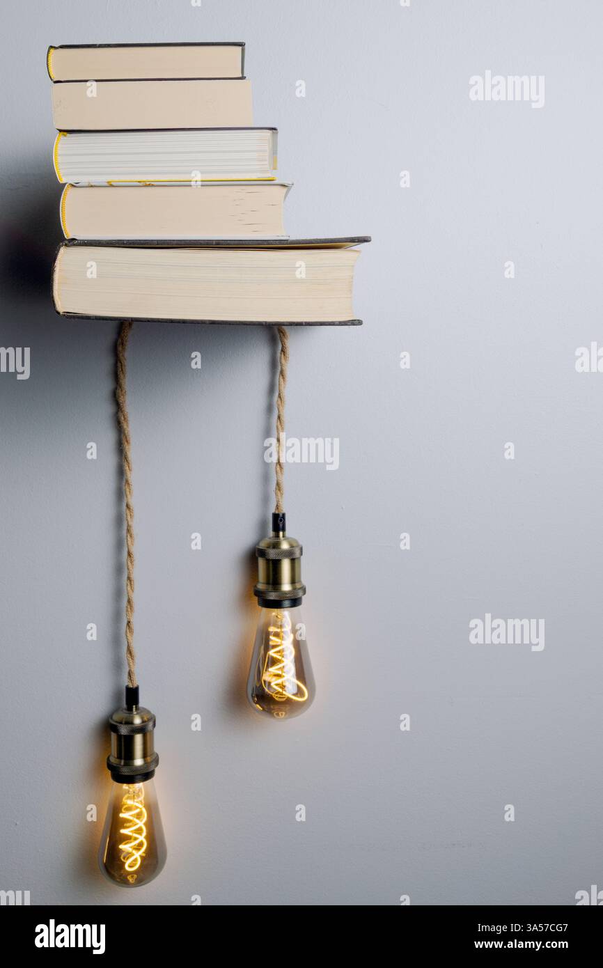 Une étagère avec des livres et deux ampoules suspendues. Les ampoules sont jaunes et les livres sont empilés les uns sur les autres. La scène s'envole Banque D'Images