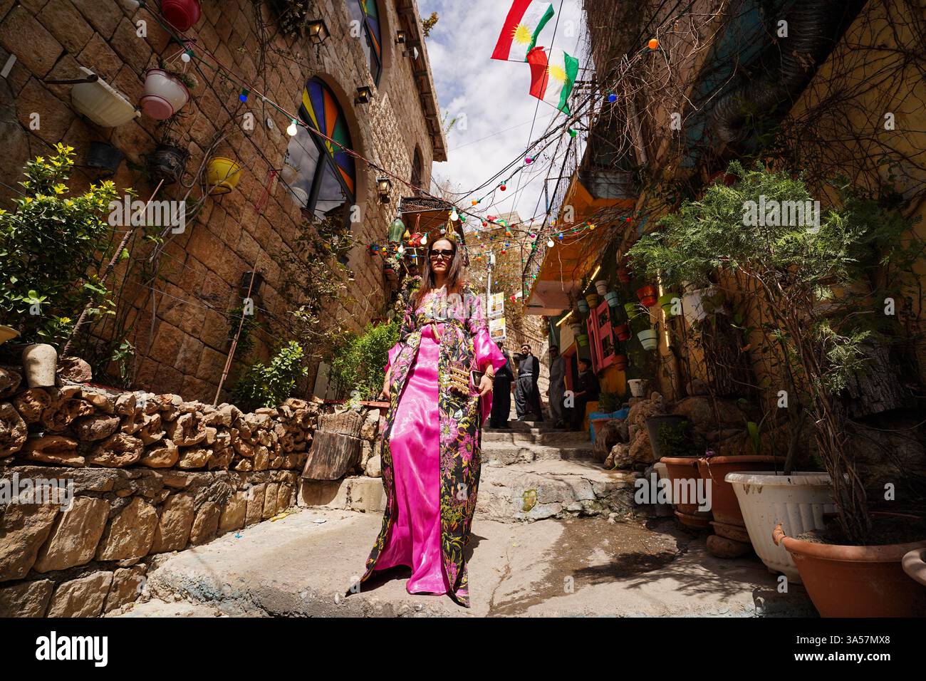 Une femme kurde irakienne vêtue de vêtements traditionnels marche dans une ruelle décorée de la ville d'Akre, dans la région du Kurdistan, pendant les célébrations du jour du Novruz, un festival marquant le premier jour du printemps, le nouvel an kurde et persan. Nowruz, également connu sous le nom de nouvel an kurde et persan, est une célébration séculaire marquant l'arrivée du printemps et le début de la nouvelle année dans le calendrier persan. Observé par des millions de personnes à travers le moyen-Orient, l'Asie centrale, et au-delà, il symbolise le renouveau, l'espoir, et le triomphe de la lumière sur les ténèbres. Le festival comprend des traditions telles que les réunions de famille, Banque D'Images
