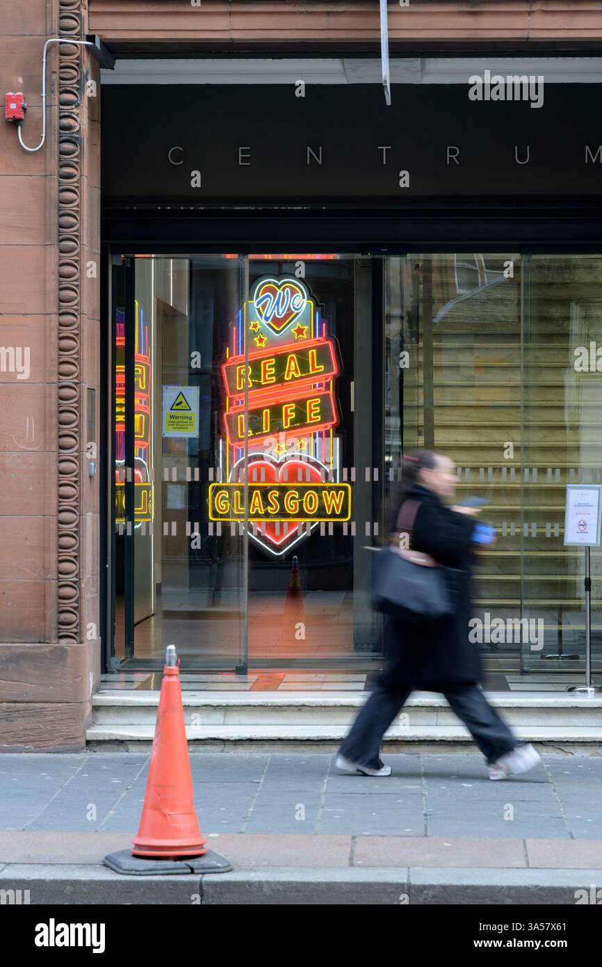 Femme passant un signe de néon We Love Real Life Glasgow, Queen Street, Glasgow, Écosse, Royaume-Uni, Europe Banque D'Images