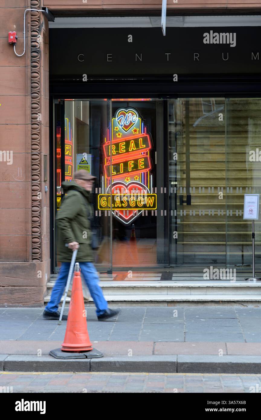 Homme passant un panneau au néon We Love Real Life Glasgow, Queen Street, Glasgow, Écosse, Royaume-Uni, Europe Banque D'Images