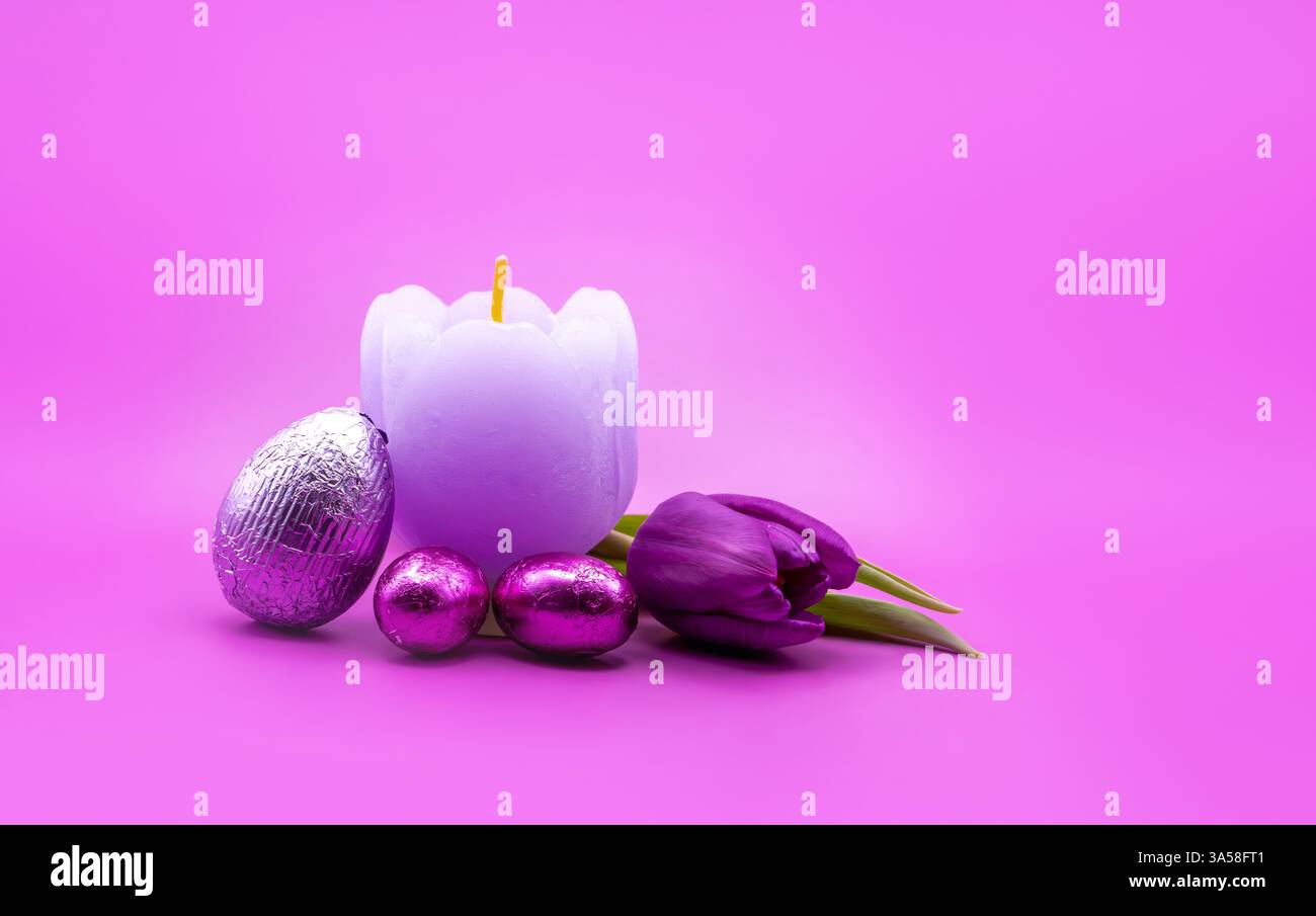 Composition de Pâques avec une bougie en forme de tulipe, des œufs enveloppés dans du papier d'aluminium et une tulipe violette sur un fond rose vif. Une nature morte parfaite pour les cartes Banque D'Images
