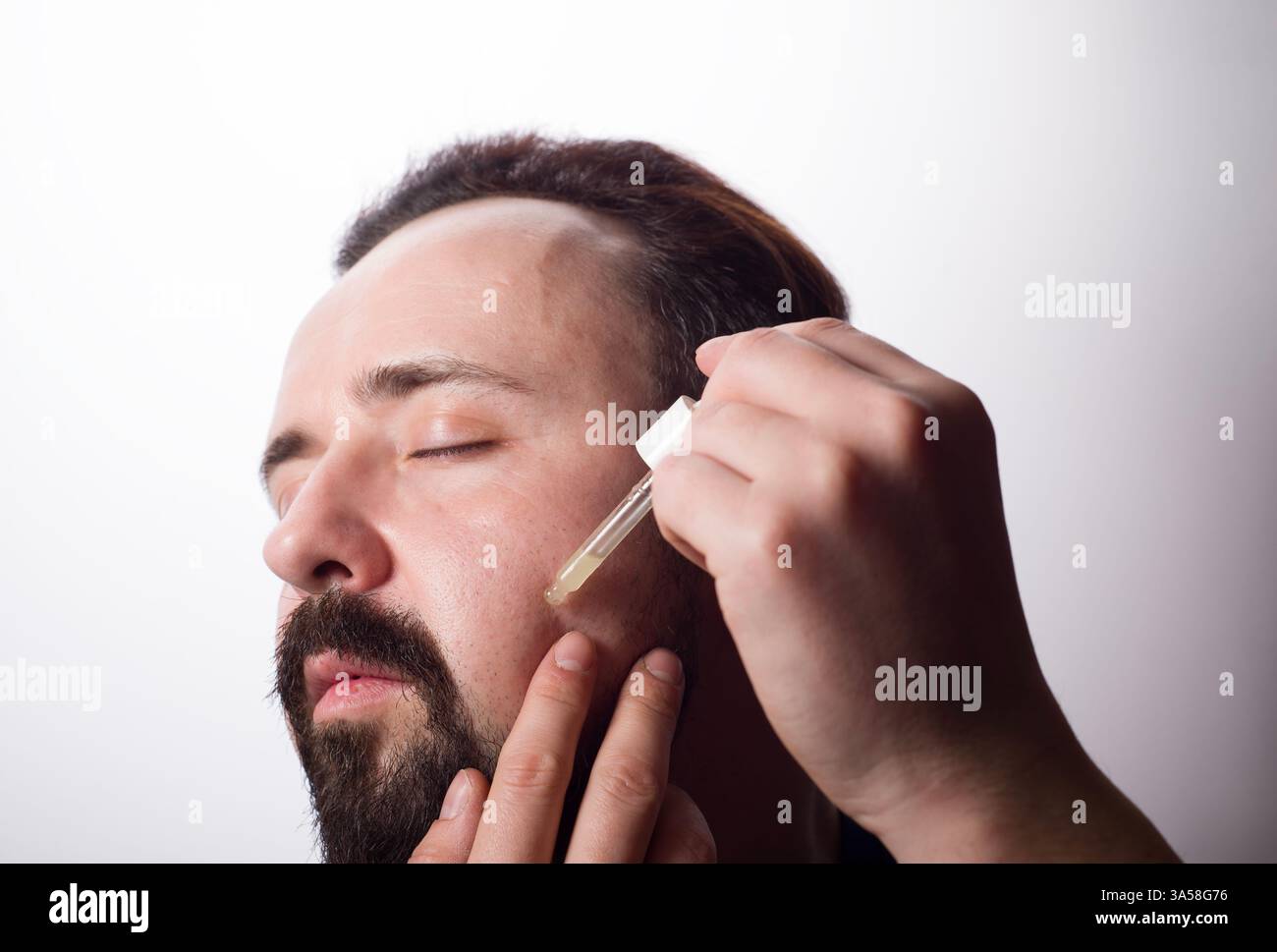 Gros plan du visage masculin et pipette avec une huile pour une croissance de barbe. Banque D'Images