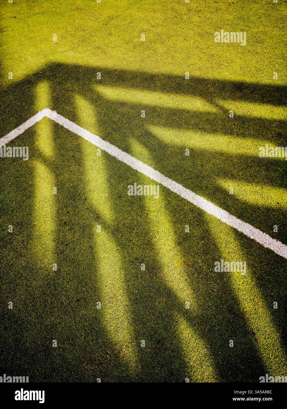 Le terrain de sport vert éclatant affiche un contraste net tandis que la lumière du soleil filtre à travers une structure, projetant des ombres complexes qui forment des formes géométriques Banque D'Images