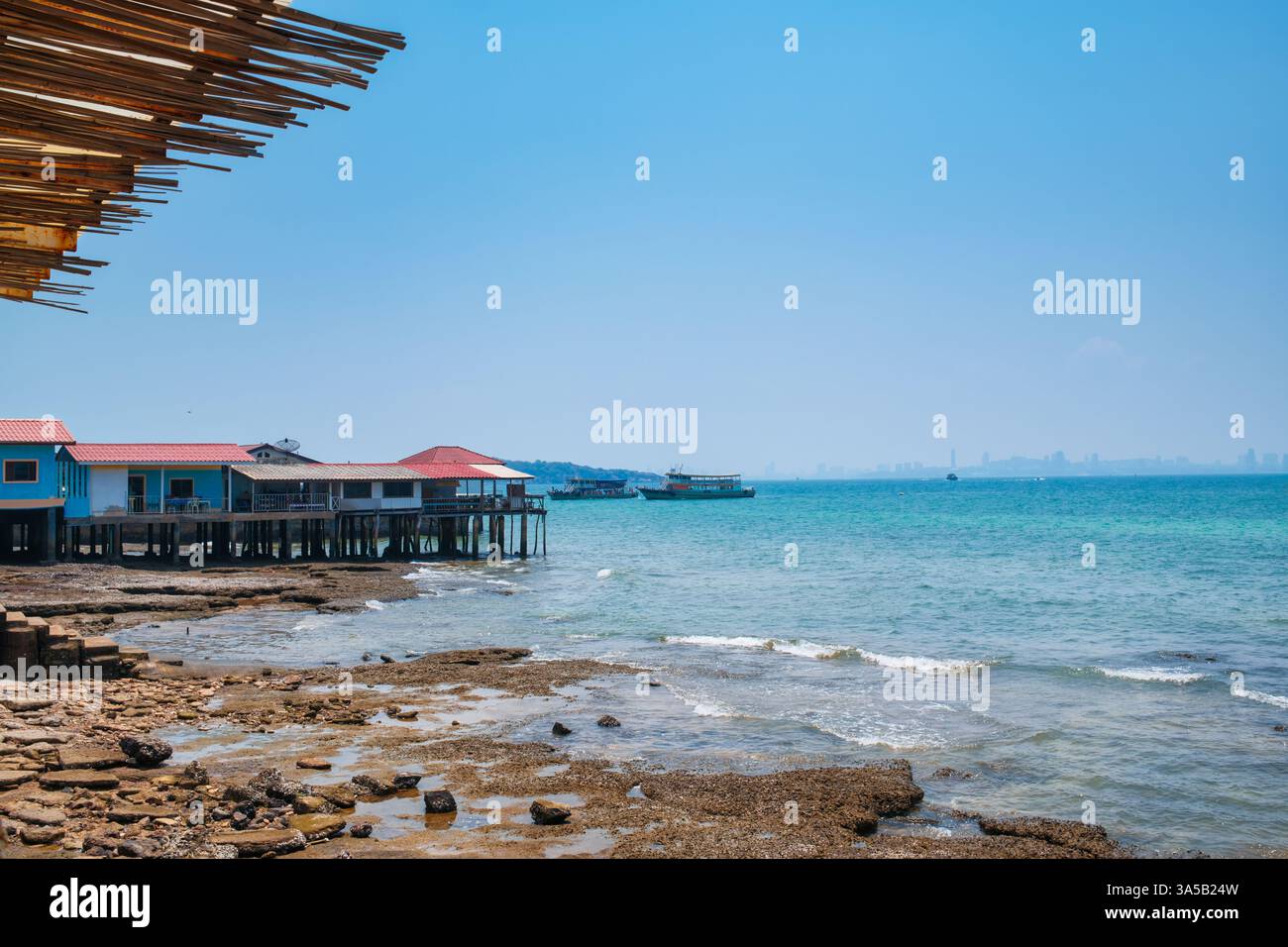 Vue sur la mer du village de pêcheurs construit sur la mer tropicale et ferry par le quai en été à Koh Larn, Chonburi, Thaïlande Banque D'Images