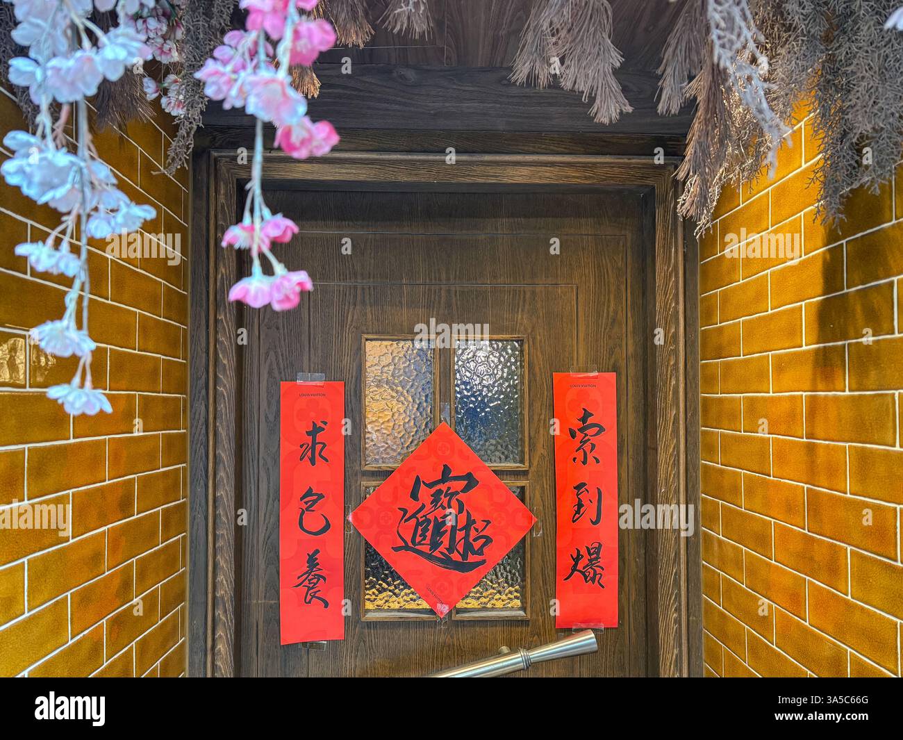 Porte décorée avec des décorations chinoises du nouvel an et des bannières rouges avec des écrits de bénédiction sur le mur de briques jaunes Banque D'Images