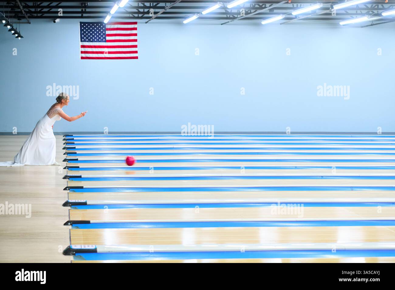 Une mariée lance une boule de bowling avec un fond bleu et un drapeau américain des États-Unis. Banque D'Images