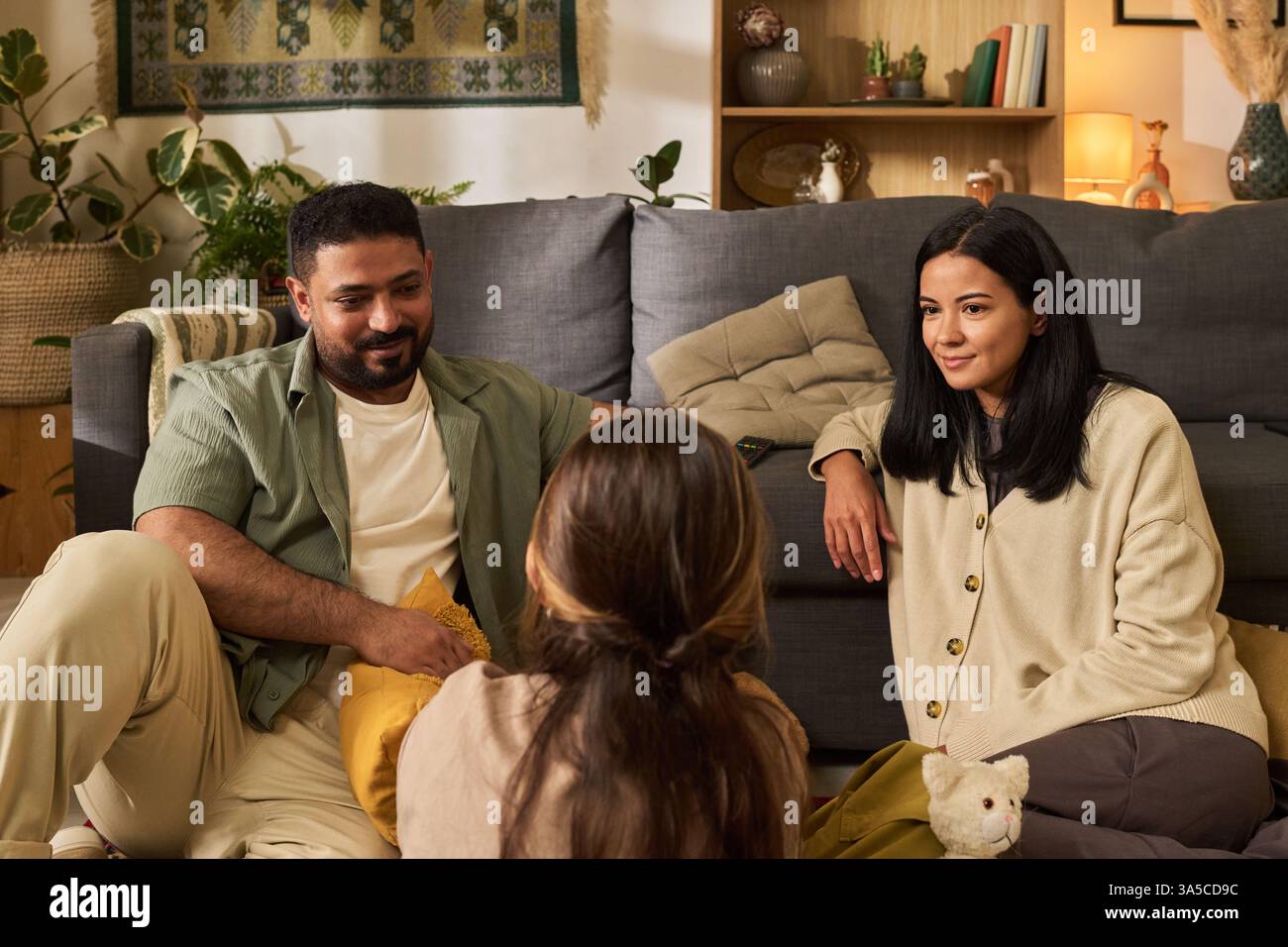 Portrait de réunion de famille dans un salon confortable. Parents s'engageant avec l'enfant tout en étant assis sur le sol avec divers éléments de décoration autour, créant une atmosphère chaleureuse et accueillante Banque D'Images