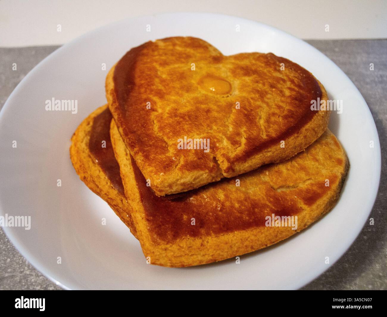 Gâteries cuites en forme de coeur, brun doré et empilées sur une assiette blanche. Un en-cas sucré et délicieux. fait pour les couples et la saint-valentin. Banque D'Images