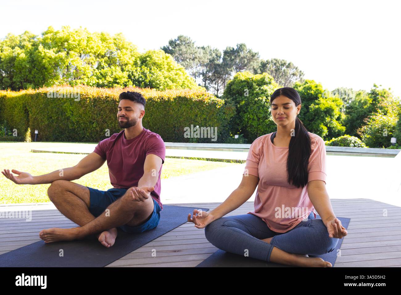 Couple méditant à l'extérieur sur des tapis de yoga, profitant d'un cadre paisible de jardin Banque D'Images