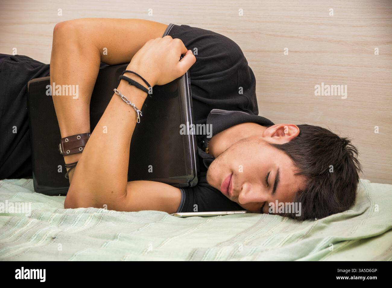 Close Up of assez jeune homme aux cheveux noirs de dormir sur le plancher ou Bed Holding laptop computer Banque D'Images