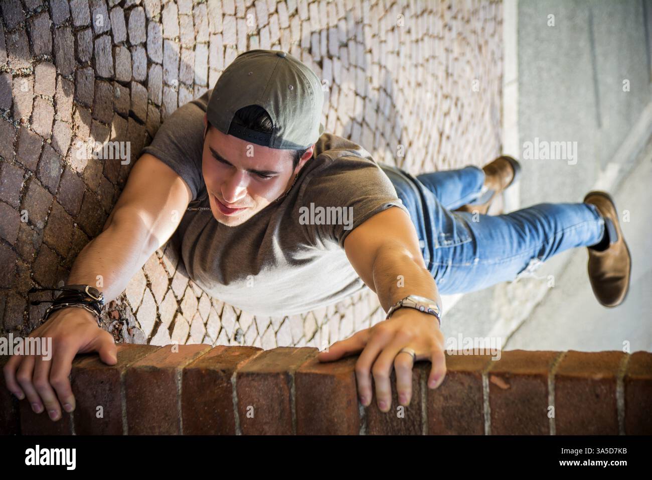 Un jeune homme suspendu à un mur de briques. Illusion d'optique prise Banque D'Images
