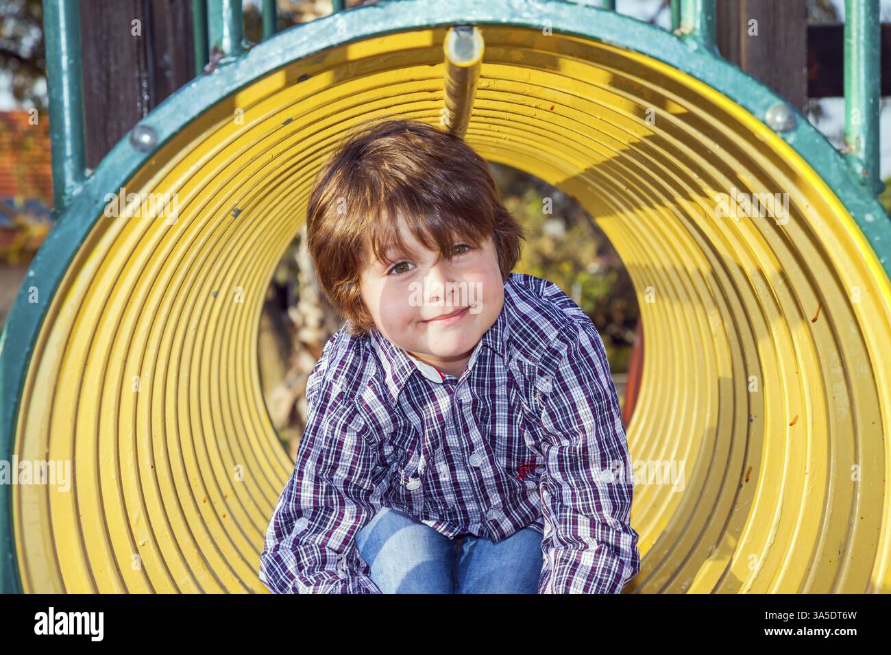 Aire de jeux pour enfants. Beau garçon charmant dans un cow-boy à carreaux rampant le long d'un passage de tuyau. Belle journée ensoleillée. Concept de publicité photo et ha Banque D'Images