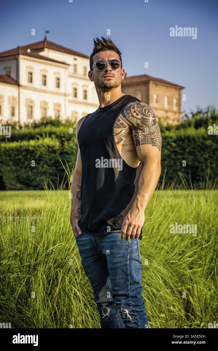 Bel homme musclé avec tatouage posant dans le jardin de luxe européen au palais royal Venaria Reale près de Turin, Italie, Europe Banque D'Images