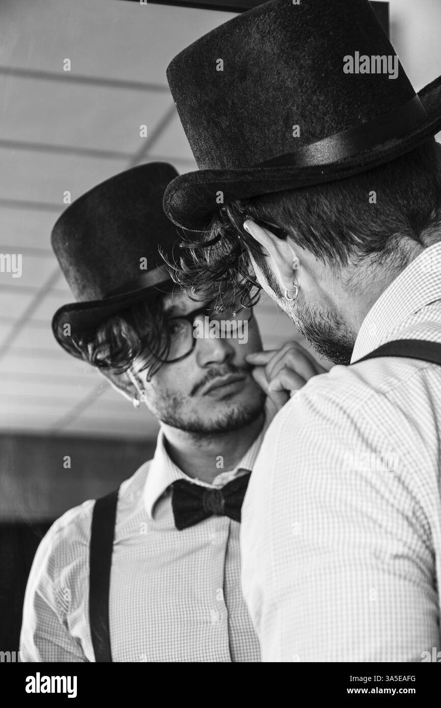 Portrait de jeune femme brune l'Homme à lunettes, chapeau, nœud papillon, bretelles et une chemise en se regardant dans un miroir. Look Vintage Banque D'Images