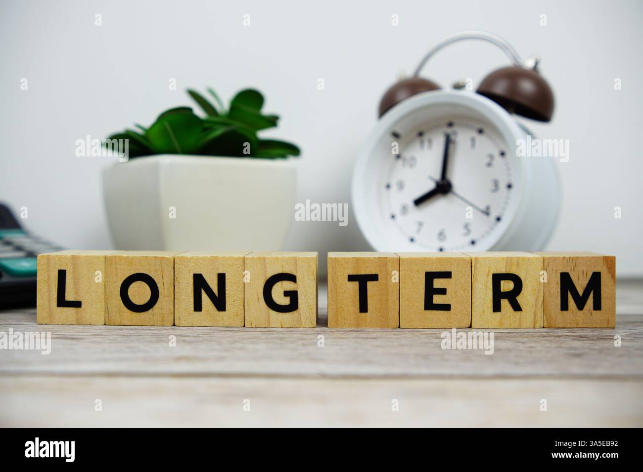 Réveil avec blocs en bois lettres de l'alphabet message texte À LONG TERME sur fond en bois Banque D'Images