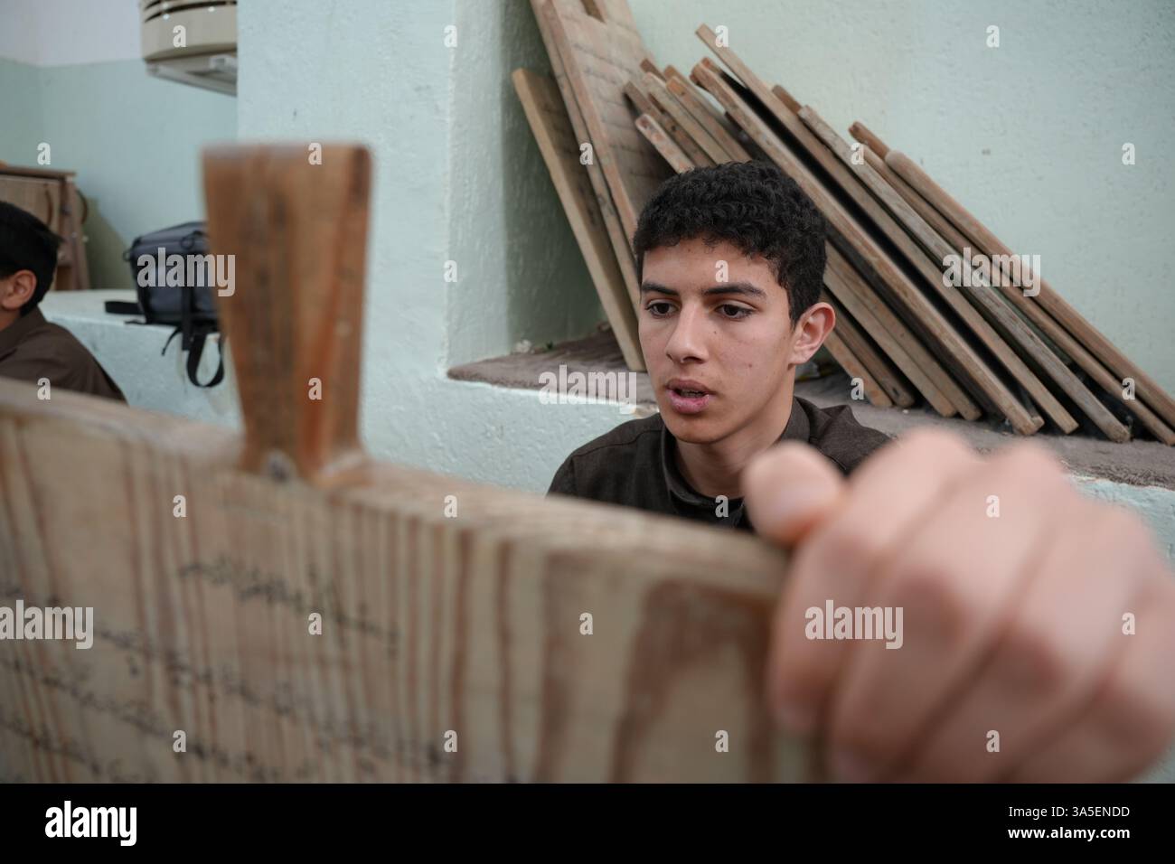 Misrata, Libye. 23 mars 2025. Un étudiant se concentre sur la lecture de versets du Saint Coran écrits sur sa tablette en bois, les enfants libyens sont assis dans une école coranique traditionnelle, inscrivant soigneusement des versets sur des tablettes en bois pendant que leur professeur les guide dans la récitation. Cette méthode séculaire, ravivée pendant le Ramadan, reste une pratique chère pour mémoriser le Saint Coran. (Photo par Islam Alatrash/SOPA images/SIPA USA) crédit : Sipa US/Alamy Live News Banque D'Images