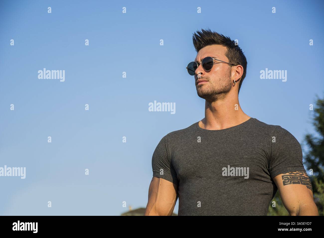 Bel homme musclé avec tatouage posant à l'extérieur contre le ciel bleu Banque D'Images