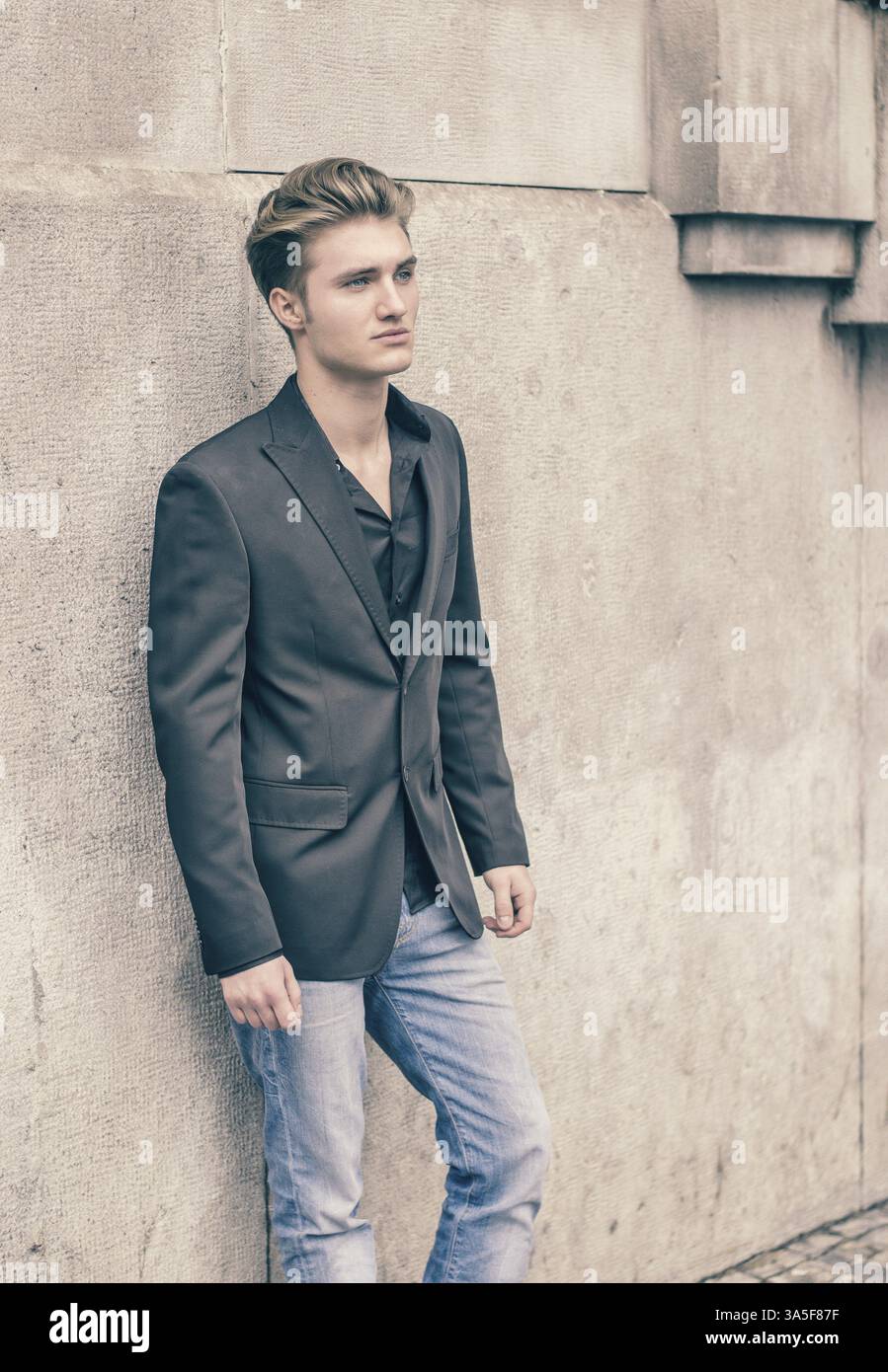 Beau jeune homme blond, yeux bleus, appuyé contre le mur blanc, pierre brute, à côté jusqu'à un Banque D'Images