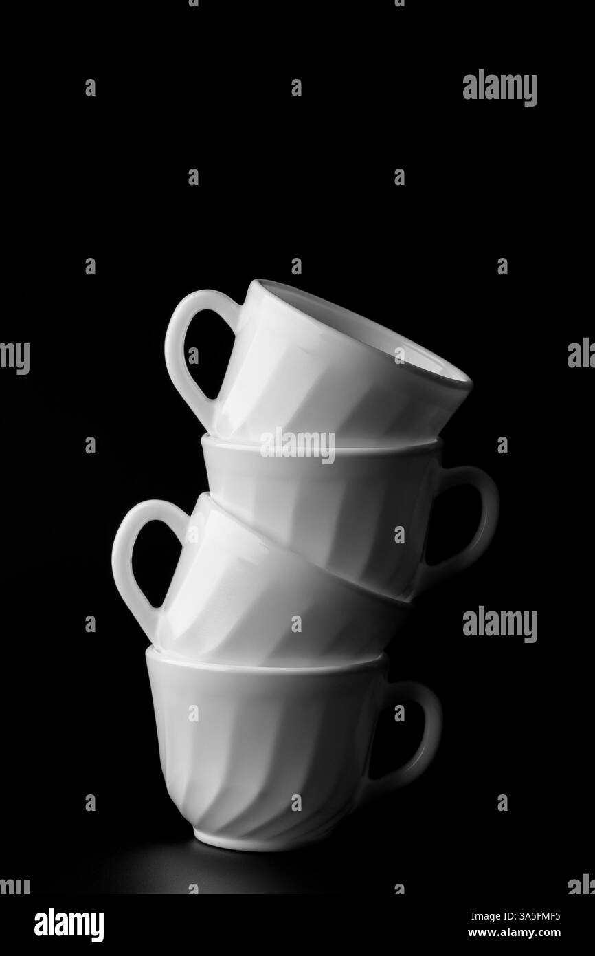 Quatre tasses en céramique blanche debout dans une pyramide sur un fond sombre. Banque D'Images Quatre tasses en céramique blanche debout dans une pyramide sur un fond sombre. Banque D'Images